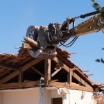 An industrial excavator tearing down the framework of an old roof corner