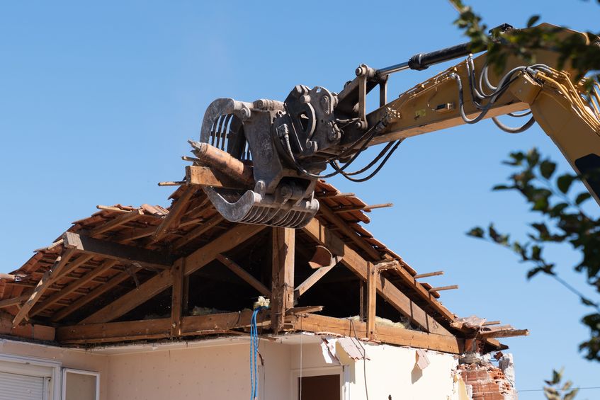An industrial excavator tearing down the framework of an old roof corner